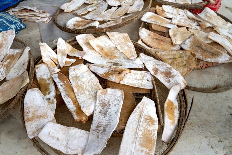 Close-up of dried fish arranged on woven trays, prepared for market sale.